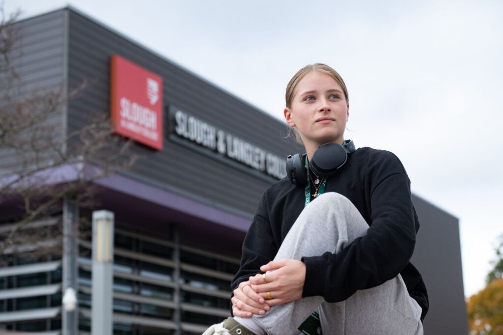Student sitting on the wall outside college looking into the distance