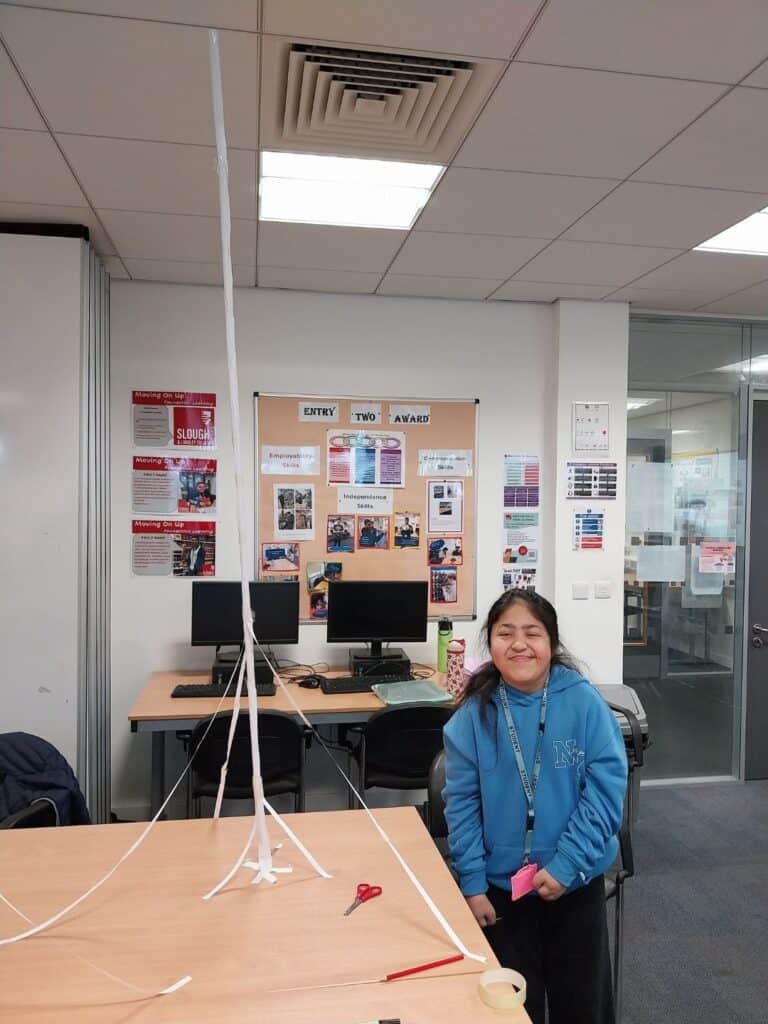 Female student stood next to their tall structure made of paper