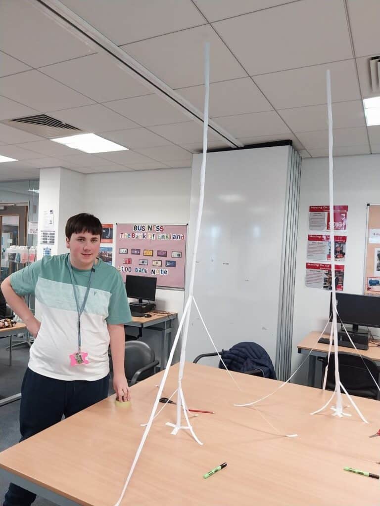 Male student stood next to their tall structure made of paper