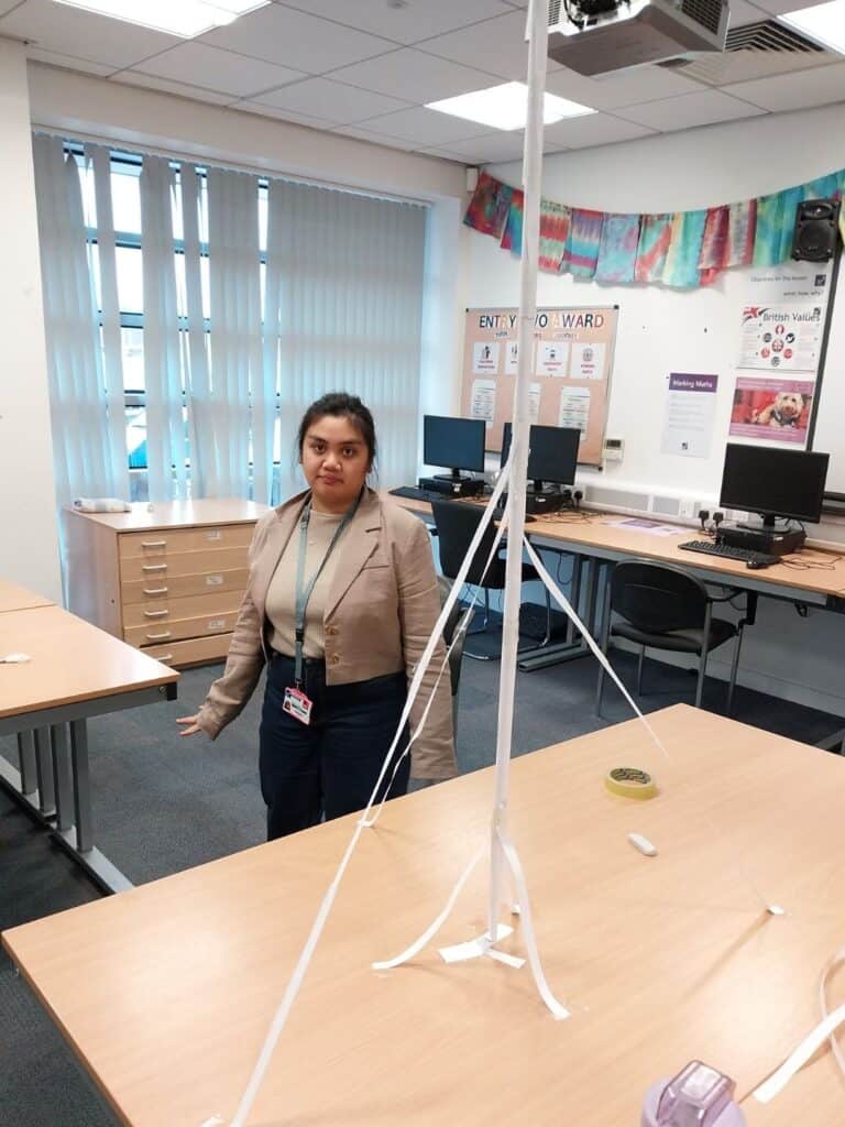 Female student stood next to their tall structure made of paper